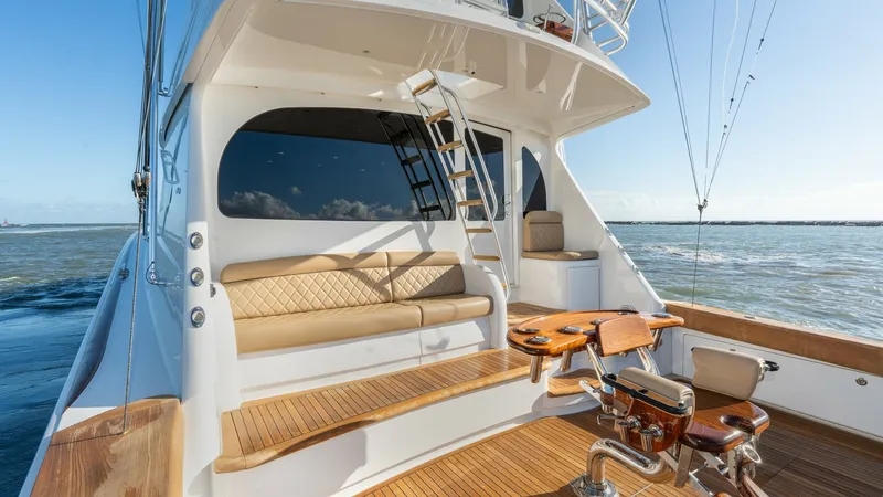 Slide: The Image of Aft Deck with Fishing Chair This image showcases the aft deck of the 2019 Viking 68 Enclosed Bridge, featuring a spacious seating area with plush, tan upholstery. The teak decking adds a touch of elegance, complemented by a professional-grade fishing chair for the avid angler. A lad - 8738051