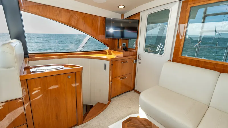 Slide: The Image of Enclosed Bridge Lounge Area The enclosed bridge lounge of the 2019 Viking 68 Enclosed Bridge offers a luxurious space with stunning ocean views. Featuring high-gloss wood cabinetry and plush seating, it combines elegance and comfort. A mounted flat-screen TV and ample natural light - 8738027