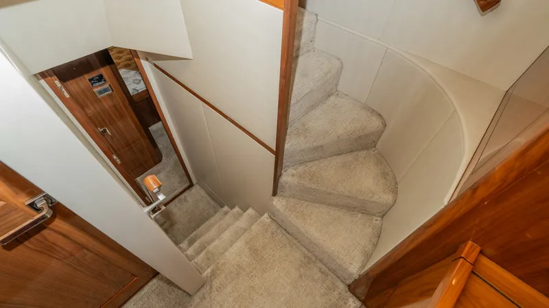 Slide: The Image of Carpeted Interior Staircase This image showcases the elegant, carpeted staircase leading to the lower deck of the 2019 Viking 68 Enclosed Bridge. The staircase features warm wood accents and soft lighting, creating a welcoming transition between levels. The design maximizes space an - 8738036