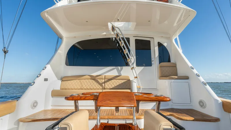 Slide: The Image of Aft Deck with Seating and Table This image showcases the aft deck of the 2019 Viking 68 Enclosed Bridge, featuring a spacious seating area with plush, tan cushions for comfort. The polished wooden table at the center adds a touch of elegance and functionality, perfect for outdoor dining - 8738054