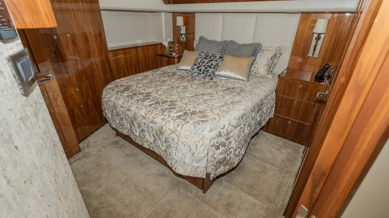 Slide: The Image of Luxurious Master Stateroom This inviting master stateroom on the 2019 Viking 68 Enclosed Bridge features a plush queen-sized bed adorned with elegant bedding. Rich wood paneling and cabinetry provide ample storage while adding warmth and sophistication to the space. Soft ambient li - 8738032