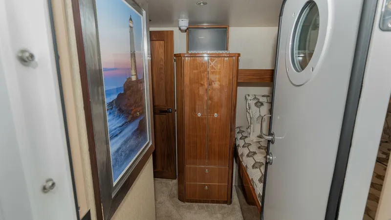 Slide: The Image of Guest Cabin Entryway This cozy guest cabin on the 2019 Viking 68 Enclosed Bridge features elegant wood cabinetry and a comfortable berth. The space is accented by nautical artwork and soft carpeting, creating a warm and inviting atmosphere. A porthole door adds a classic touc - 8738042