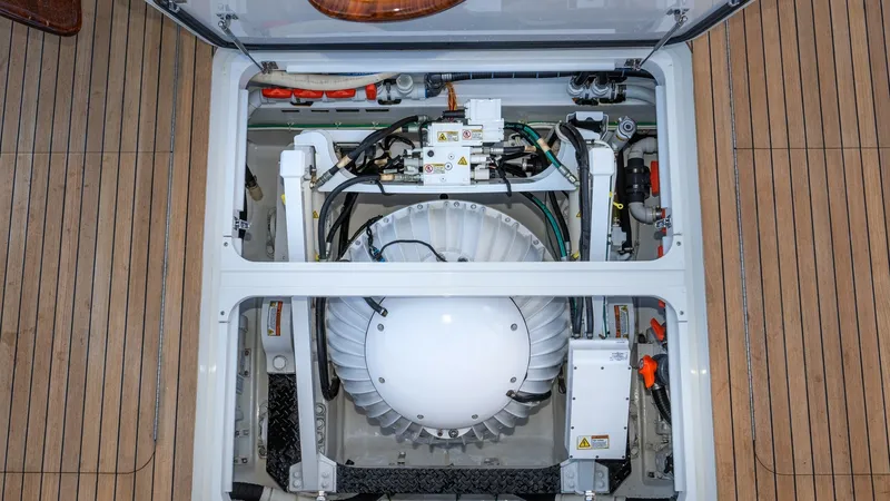 Slide: The Image of Engine Room Access Hatch This image showcases the engine room access hatch on the 2019 Viking 68 Enclosed Bridge. The meticulously organized space features advanced mechanical systems essential for optimal yacht performance. The teak decking adds a touch of elegance to the practi - 8738047