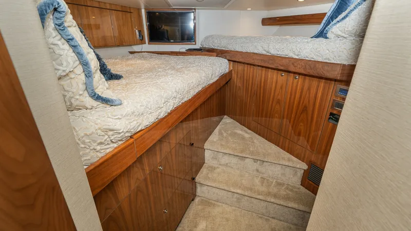 Slide: The Image of Guest Cabin with Twin Berths This cozy guest cabin on the 2019 Viking 68 Enclosed Bridge features twin berths with plush bedding and elegant wood paneling. The soft carpeted steps provide easy access, complementing the warm and inviting atmosphere. Recessed lighting and a mounted TV - 8738028