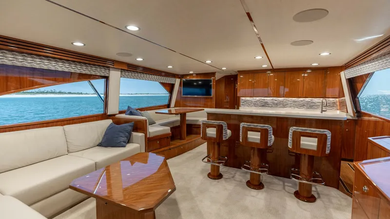 Slide: The Image of Spacious Salon with Galley Bar This elegant salon in the 2019 Viking 68 Convertible 'Gas Money' features a luxurious blend of comfort and style. The open-plan layout includes a plush L-shaped sofa, a polished wood coffee table, and a galley with a bar area, complete with high-back stoo - 8679260