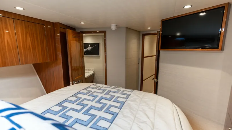 Slide: The Image of Master Stateroom with Ensuite Access The master stateroom of the 2019 Viking 68 Convertible features a plush, patterned bedspread and elegant wood cabinetry, providing a warm and inviting ambiance. The room is equipped with a wall-mounted flat screen TV for entertainment. Access to the ensui - 8679274