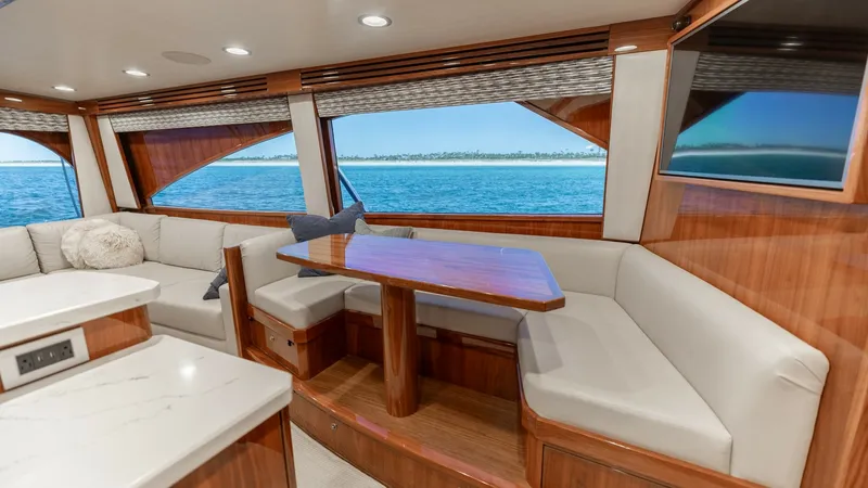 Slide: The Image of Salon Dining Area with Ocean View The salon dining area of the 2019 Viking 68 Convertible features a spacious L-shaped seating arrangement with plush cushions, perfect for entertaining or relaxing. The beautifully crafted wooden table complements the luxurious wood finishes throughout the - 8679264