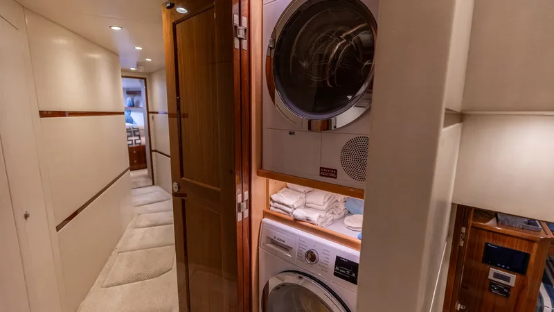 Slide: The Image of Hallway with Laundry Area This image showcases the sleek hallway of the 2019 Viking 68 Convertible, featuring an integrated laundry area. The stacked washer and dryer are neatly tucked behind elegant wood-paneled doors, providing convenience without compromising on style. Soft, am - 8679267