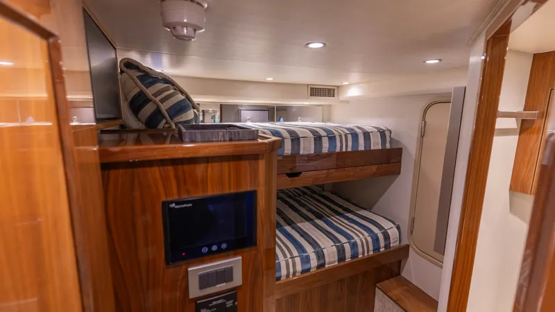 Slide: The Image of Guest Cabin with Bunk Beds This cozy guest cabin on the 2019 Viking 68 Convertible features stylish bunk beds with striped bedding. The warm wood finishes and built-in storage provide a practical and inviting space. Recessed lighting enhances the room's ambiance, making it comforta - 8679279