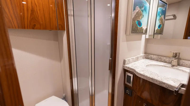 Slide: The Image of Luxurious En-Suite Bathroom This elegant en-suite bathroom on the Viking 68 Convertible features high-gloss wood cabinetry and a sleek granite countertop. The frosted glass shower door adds a touch of modern sophistication, while ample lighting ensures a bright and inviting space. T - 8679283