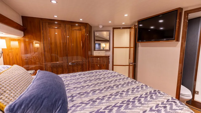 Slide: The Image of Master Stateroom with En-Suite This luxurious master stateroom on the Viking 68 Convertible features a plush queen-sized bed adorned with elegant bedding. The space is enhanced by rich wood cabinetry and ambient recessed lighting, creating a cozy yet sophisticated atmosphere. A wall-mo - 8679270