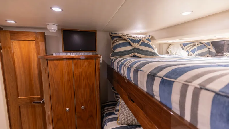 Slide: The Image of Guest Cabin with Bunk Beds This cozy guest cabin on the 2019 Viking 68 Convertible features comfortable bunk beds with stylish striped bedding. The warm wood finishes of the cabinetry and door add a touch of elegance, while recessed lighting creates a welcoming ambiance. A mounted - 8679281