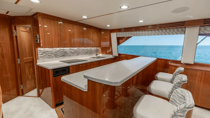 Slide: The Image of Galley with Breakfast Bar This stylish galley on the 2019 Viking 68 Convertible features a sleek breakfast bar with plush seating, perfect for casual dining. The high-gloss wood cabinetry complements the modern backsplash, creating a sophisticated look. Large windows provide stunn - 8679265