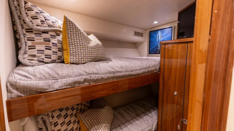 Slide: The Image of Guest Stateroom with Bunk Beds This cozy guest stateroom on the 2019 Viking 68 Convertible features comfortable bunk beds with plush bedding and stylish accent pillows. The warm wood cabinetry provides ample storage space, while recessed lighting creates a welcoming ambiance. A framed - 8679276