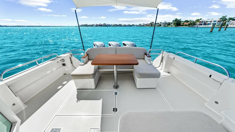 Slide: The Image of Spacious Aft Deck with Seating Area The aft deck of the 2022 Back Cove 390, 'Risk and Reward', showcases a spacious seating area with plush, cushioned benches arranged around a versatile wooden table. The area is shaded by a sleek canopy, providing comfort and style for outdoor dining or re - 8738145