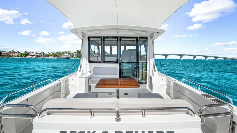 Slide: The Image of Aft Deck with Seating Area The aft deck of the 2022 Back Cove 390, 'Risk and Reward', features a spacious seating area with plush cushions and a stylish wooden table, perfect for socializing or dining al fresco. The deck is partially covered, providing shade while maintaining an op - 8738123