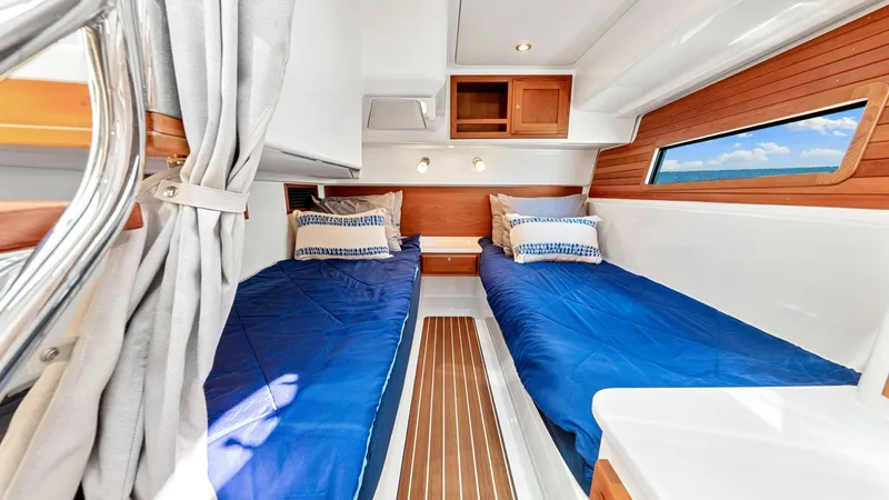 Slide: The Image of Twin Cabin with Port Window View The twin cabin features parallel berths adorned with plush blue bedding, providing a comfortable sleeping area. Rich wooden accents and a sleek, modern design enhance the room's elegance. A large port window offers natural light and picturesque views, cre - 8738141