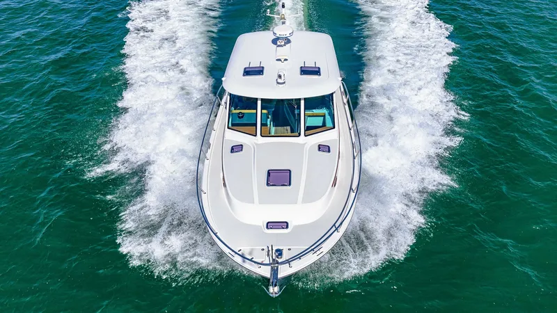Slide: The Image of Aerial View of Bow Underway The Back Cove 390, 'Risk and Reward', slices through the water with elegance and power. The sleek bow design and pristine white deck are highlighted as the vessel glides across the sea, leaving a dynamic wake. Large windows provide panoramic views and amp - 8738167
