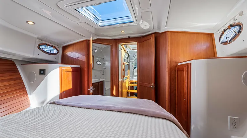 Slide: The Image of Master Stateroom with Skylight The master stateroom offers a spacious and inviting retreat, featuring a plush double bed with elegant bedding. Rich wood finishes and ample natural light from the overhead skylight and portholes create a warm and airy ambiance. The thoughtful layout incl - 8738138