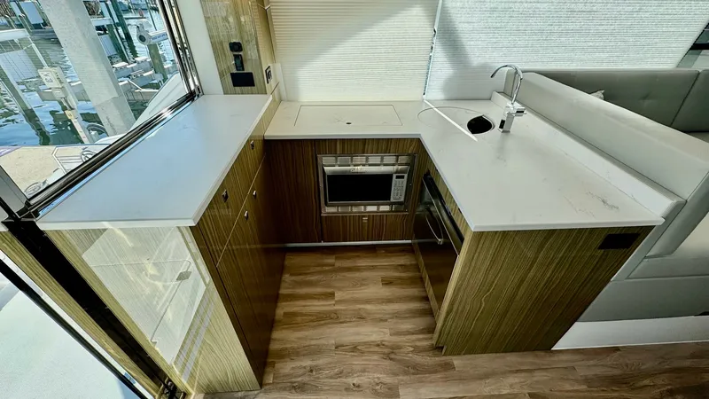 Slide: The Image of Modern Galley with Scenic Views This sleek and modern galley on the 2024 Cruisers Yachts 50 Cantius features elegant wood cabinetry and expansive countertops, ideal for culinary enthusiasts. The large windows provide ample natural light and stunning marina views, enhancing the space's o - 8737984