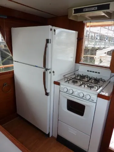 Slide: The Image of 1968 Monk 56 Flushdeck kitchen with white fridge and stove, wooden interior, and window blinds. - 36