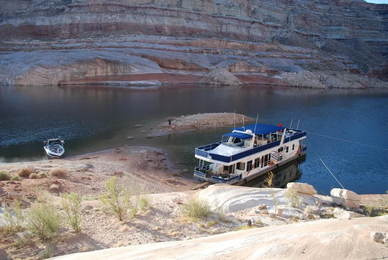 Slide: The Image of Houseboat and speedboat docked on a serene lake surrounded by rocky cliffs. - 12
