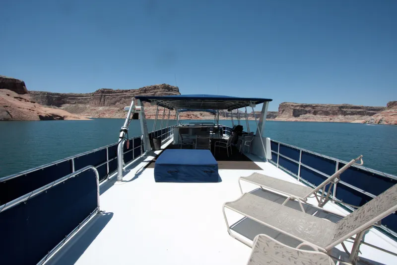 Slide: The Image of Houseboat on a serene lake with lounge chairs, clear skies, and rocky landscape. - 14