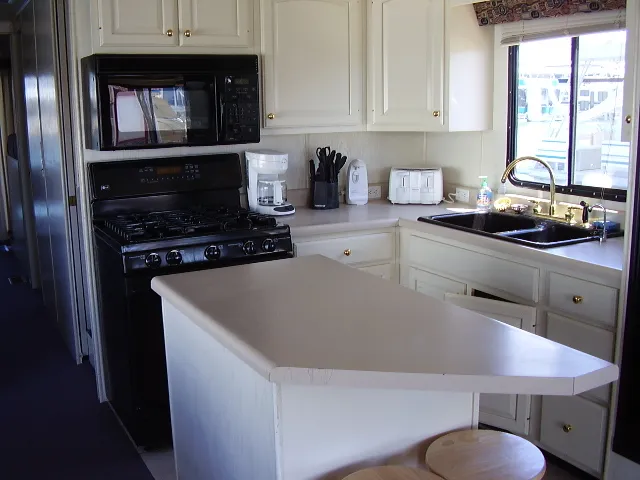 Slide: The Image of 1998 Jamestowner Widebody Multi Owner Houseboat kitchen with white cabinets and black appliances. - 2