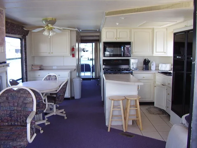 Slide: The Image of 1998 Jamestowner Widebody Multi Owner Houseboat kitchen and dining area with white cabinets and purple carpet. - 3
