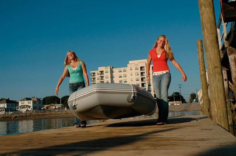 Slide: The Image of Two women carrying an Achilles LEX-77 inflatable boat on a dock, 2024 model. - 3