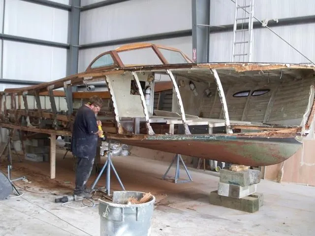 Slide: The Image of 1956 Emancipator cruiser under restoration in a workshop, with a person working on the hull. - 11