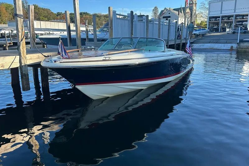 Slide: The Image of 2013 Chris-Craft Corsair 25 boat docked in a marina, reflecting on calm water. - 2