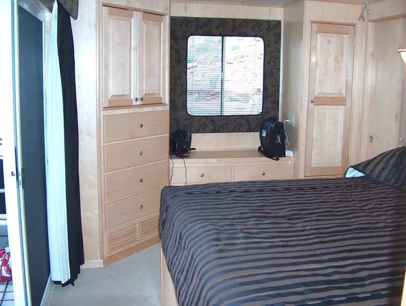 Slide: The Image of 2005 Stardust Cruisers Multi Owner Houseboat bedroom with wooden cabinets and striped bedding. - 2