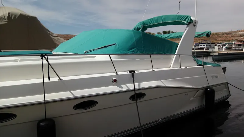 Slide: The Image of 1994 Cruisers Yachts 3672 Express boat with white and green seating by the water. - 7