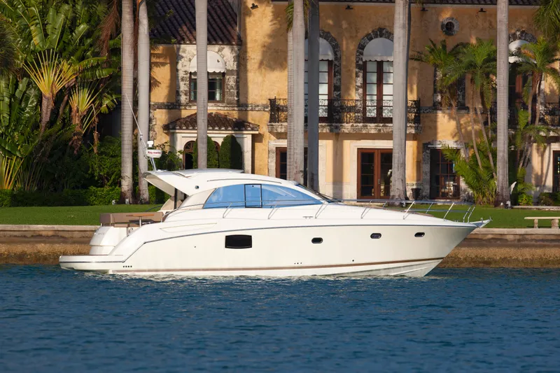 Slide: The Image of 2012 Prestige 440S yacht cruising near a luxurious waterfront villa. - 2