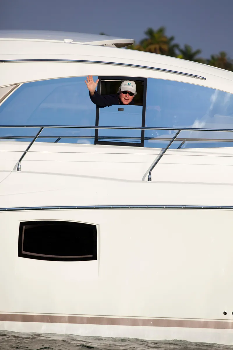 Slide: The Image of Person waving from a 2012 Prestige 440S yacht window, with palm trees in the background. - 23