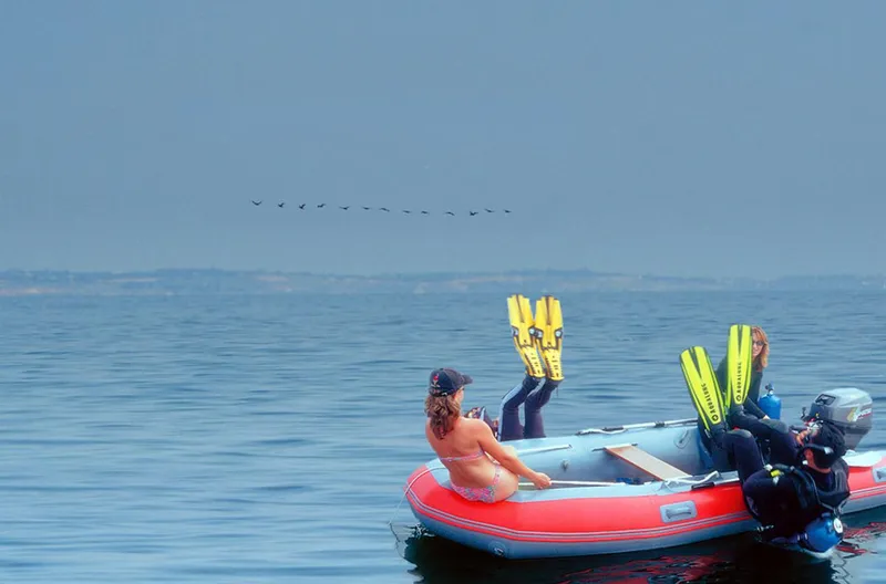 Slide: The Image of People with flippers relaxing on an Achilles SGX-132 inflatable boat, 2024 model, in calm waters. - 3