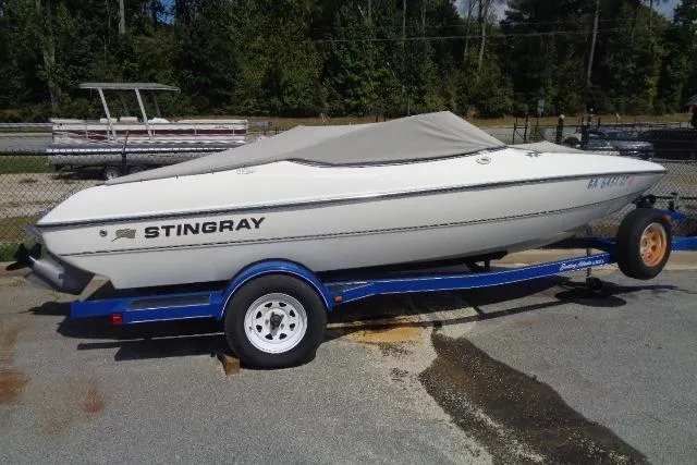 Slide: The Image of 2005 Stingray 180RX boat on a blue trailer, covered and parked outdoors. - 1
