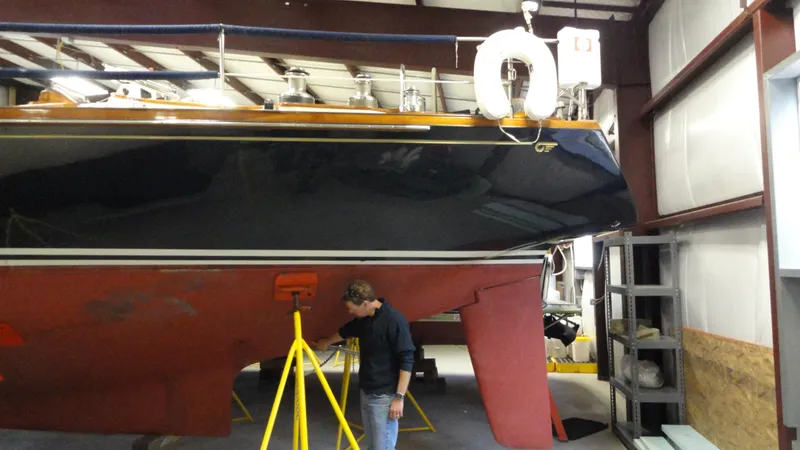 Slide: The Image of 1980 Hinckley 43 sailboat in a workshop, with a person inspecting the hull. - 43
