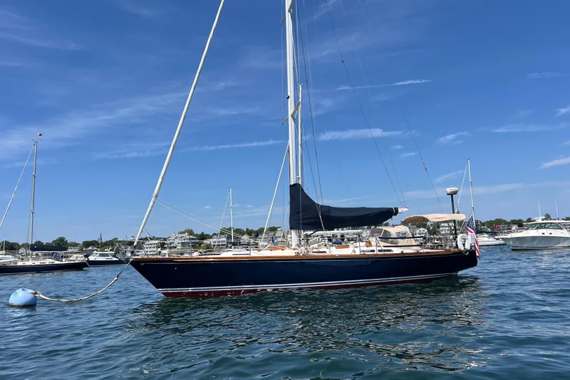 Slide: The Image of 1980 Hinckley 43 sailboat anchored in a scenic harbor under a clear blue sky. - 60