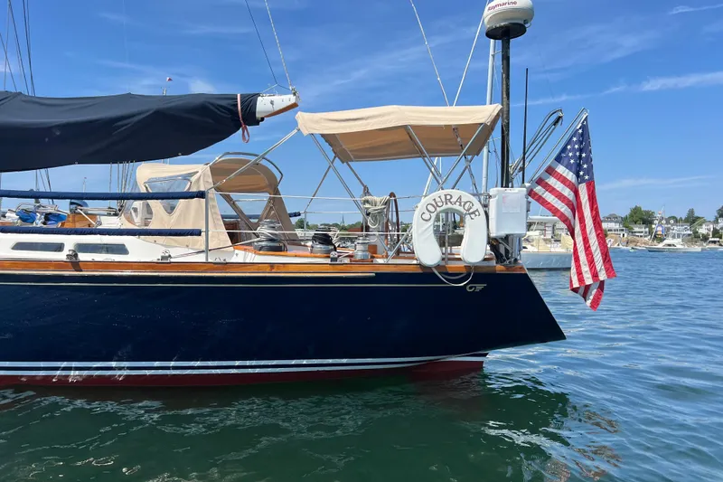 Slide: The Image of 1980 Hinckley 43 sailboat with American flag, docked in a sunny marina. - 57