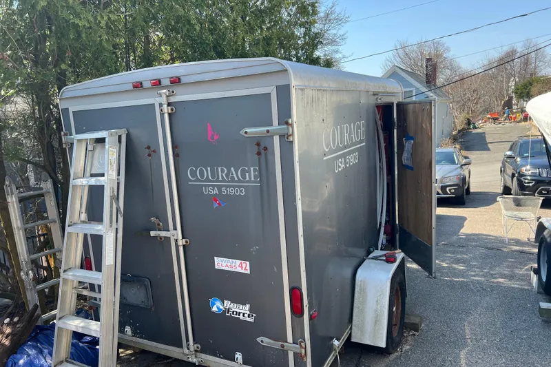 Slide: The Image of Trailer labeled "Courage USA 51903" with ladder, parked outdoors near vehicles. - 64