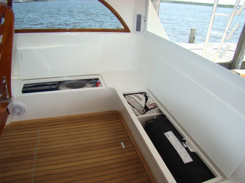 Slide: The Image of 2024 Jersey Cape 47 Custom Hardtop boat interior with storage compartments and wooden flooring. - 14