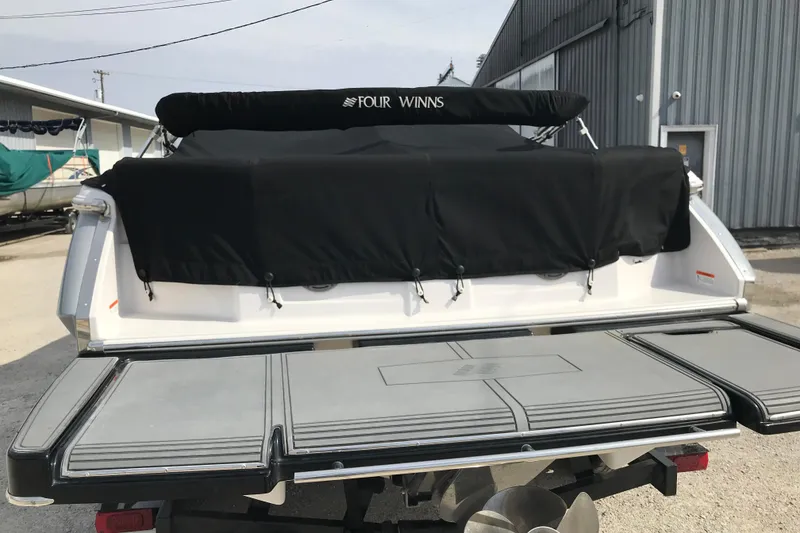 Slide: The Image of 2015 Four Winns H230 boat with black cover, docked near a warehouse. - 4