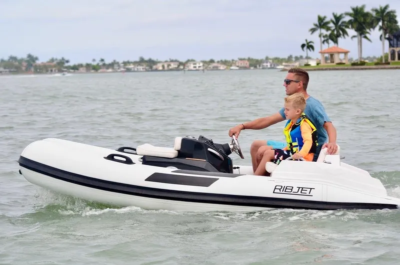 Slide: The Image of Father and son riding a 2023 Ribjet 10 boat on a calm lake. - 10