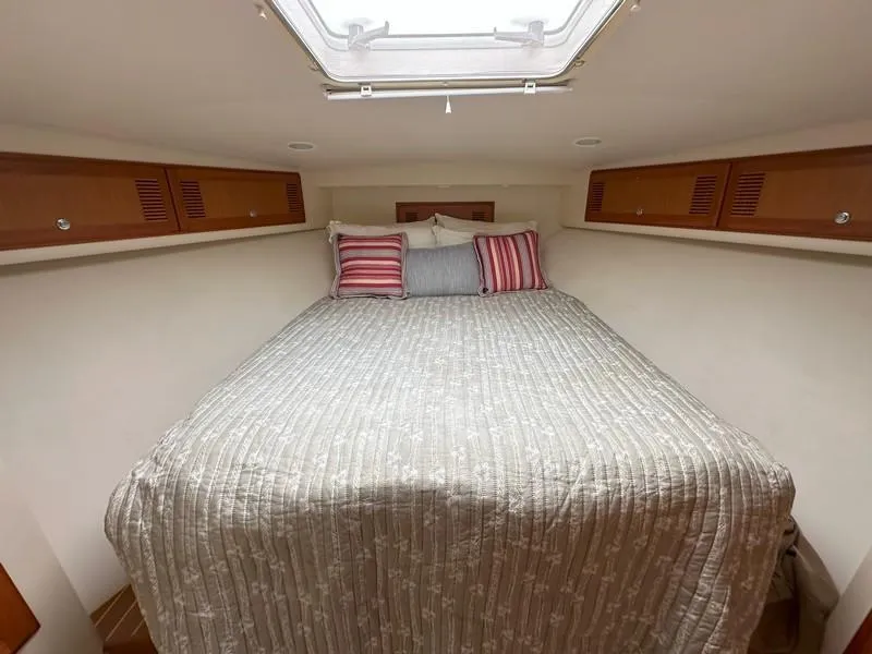 Slide: The Image of 2004 Cabo Express cabin with cozy bed, striped pillows, and wooden storage cabinets. - 42