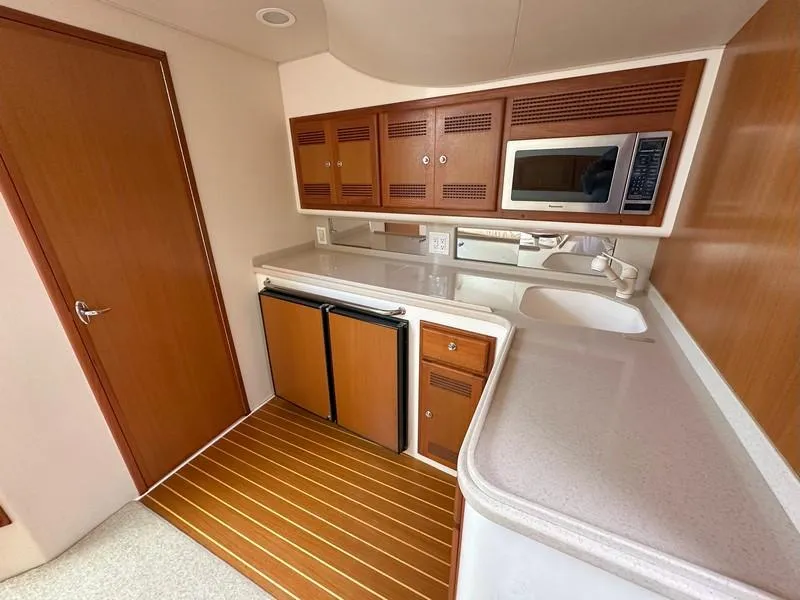 Slide: The Image of 2004 Cabo Express yacht kitchen with wood cabinets, microwave, and compact fridge. - 46