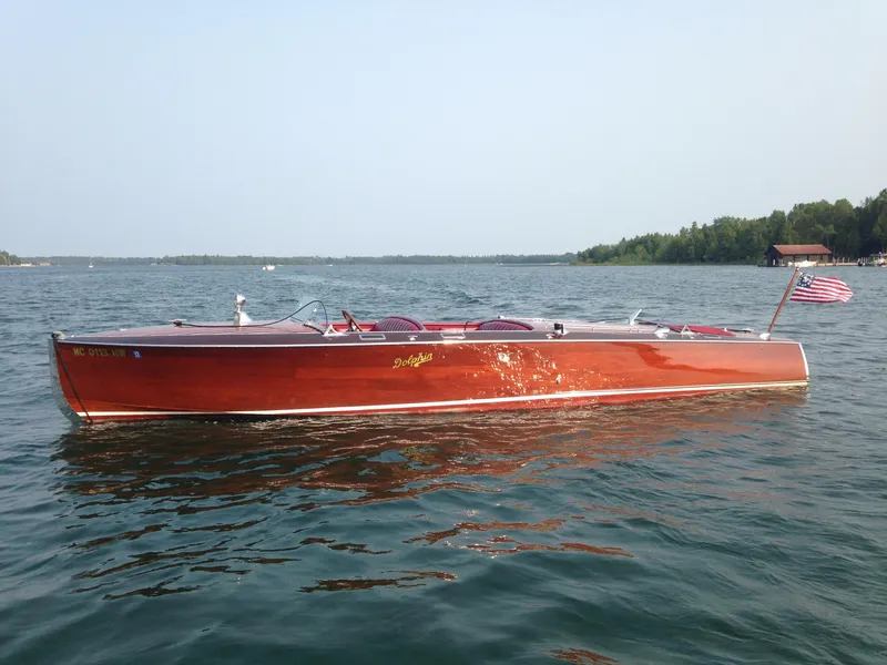 The Image of 1928 Hacker-Craft Dolphin boat on serene lake with American flag. - 1