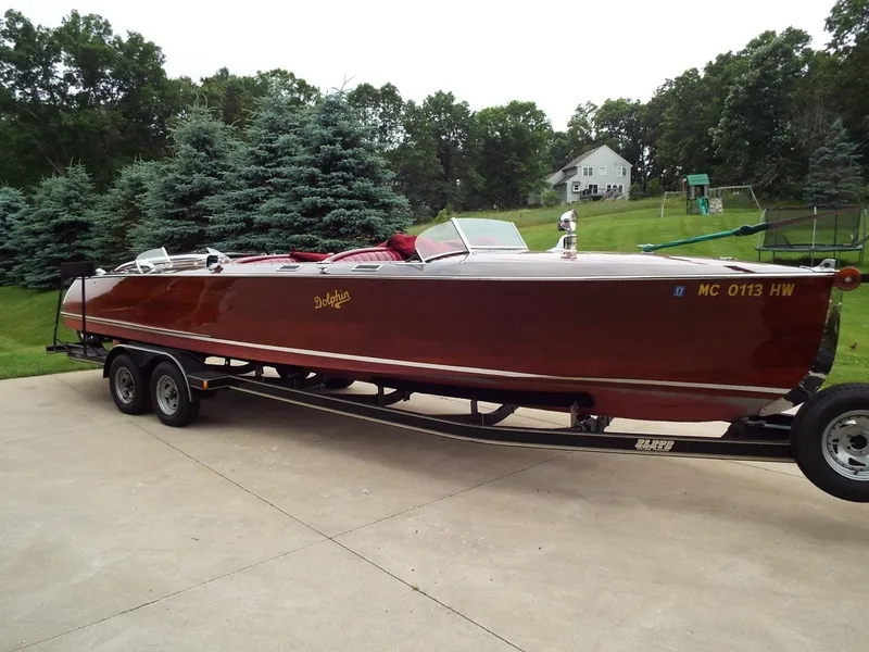 Slide: The Image of 1928 Hacker-Craft Dolphin boat on trailer, parked in driveway with trees in background. - 4