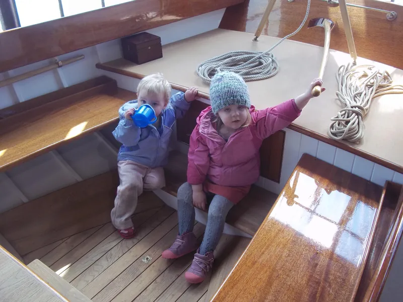Slide: The Image of Two children sitting on a 2011 Herreshoff Fish Class boat, surrounded by wooden interior and ropes. - 6